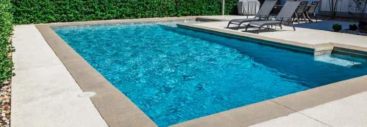 Ein Pool mit Liegestühlen, umgeben von einer dichten Hecke.